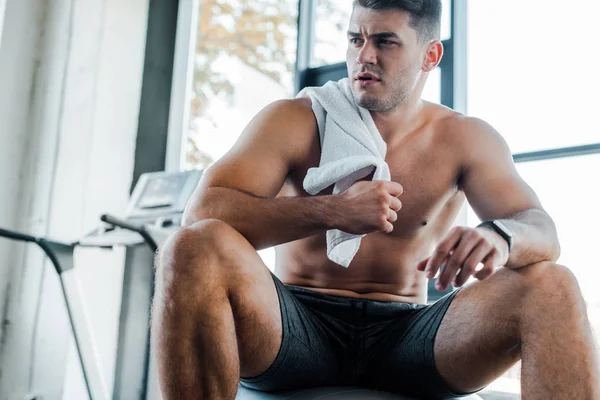 Handsome sportsman sitting and holding towel in sports center — Stock Photo