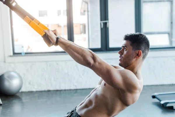 Side view of handsome sportsman working out on suspension trainer in sports center — Stock Photo