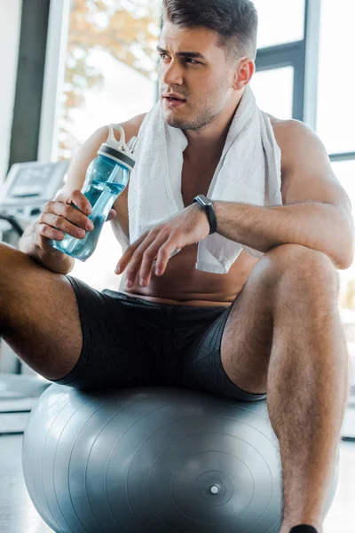 Deportista sentado en la pelota de fitness y la celebración de la botella de deportes en el centro deportivo - foto de stock