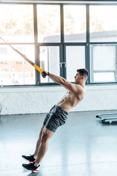 Side view of handsome sportsman working out on suspension trainer in sports center — Stock Photo
