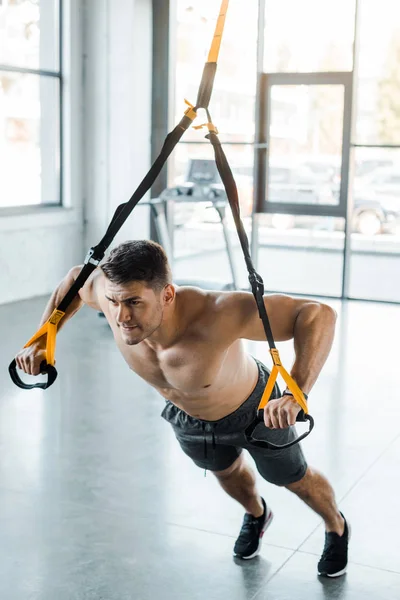 Handsome sportsman working out on suspension trainer in sports center — Stock Photo