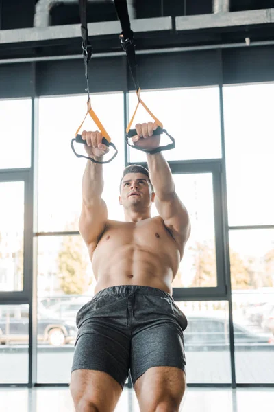 Handsome sportsman working out on suspension trainer in sports center — Stock Photo