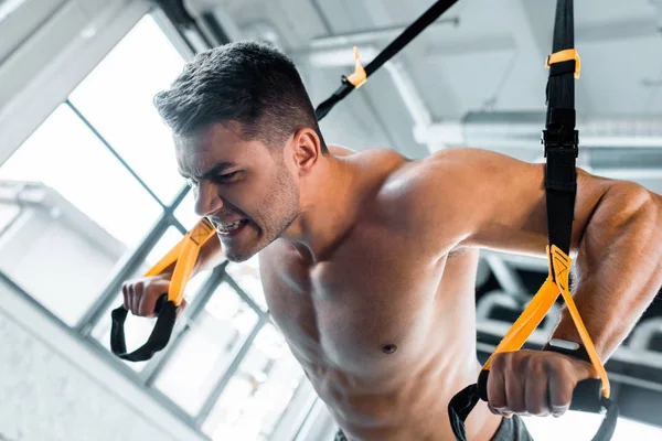 Handsome sportsman working out on suspension trainer in sports center — Stock Photo