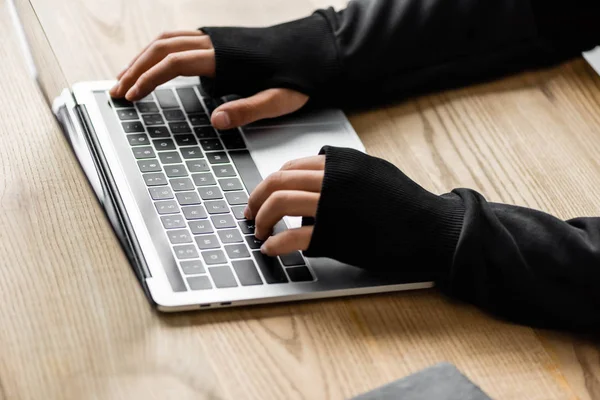 Cropped view of hacker sitting at table and using laptop — Stock Photo