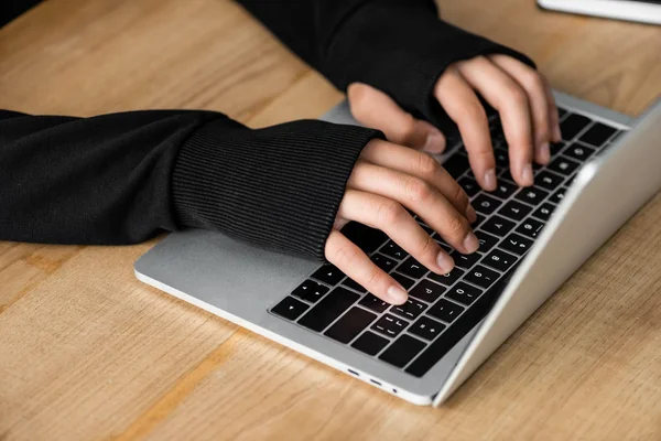 Vista recortada de hacker sentado en la mesa y el uso de ordenador portátil - foto de stock