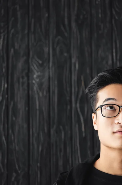 Vista ritagliata di uomo asiatico in occhiali guardando su su sfondo di legno — Foto stock