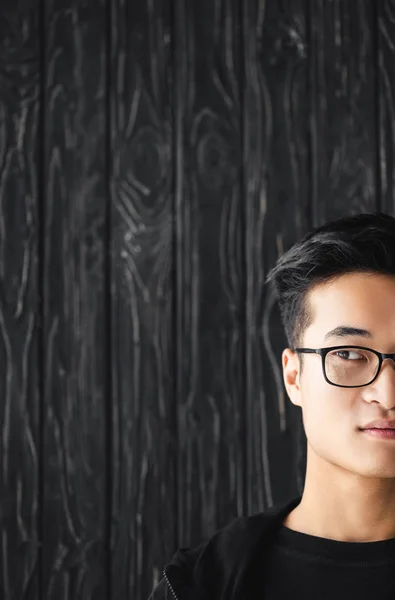 Обрезанный вид азиатского человека в очках, смотрящего в сторону на деревянном фоне — стоковое фото
