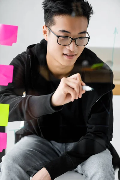 Smiling asian seo manager in glasses painting arrow on glass — Stock Photo