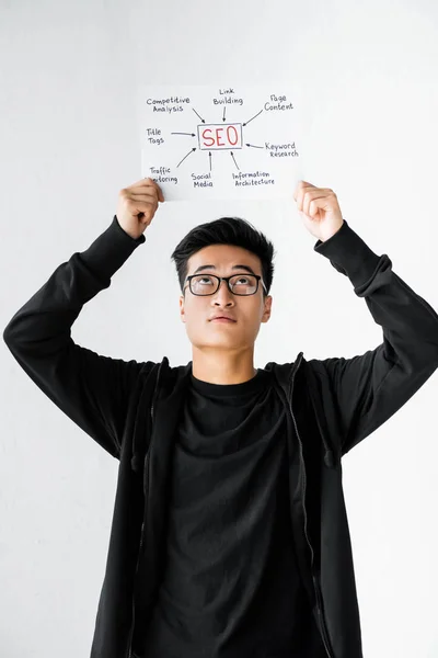 Азіатський менеджер сео, який тримає і дивиться на папір з концептуальними словами сео — стокове фото