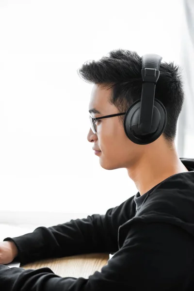 Side view of asian hacker in headphones sitting at table — Stock Photo