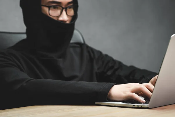 Selektiver Fokus asiatischer Hacker mit verschleiertem Gesicht mit Laptop und am Tisch sitzend — Stockfoto