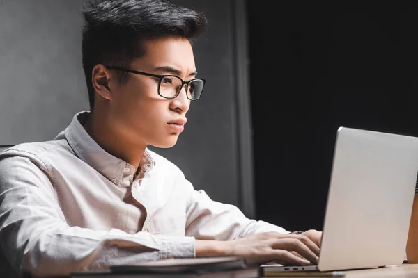 Asiático seo gerente sentado en mesa y usando laptop - foto de stock