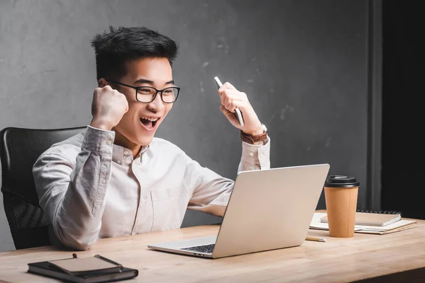 Lächelnder asiatischer SEO-Manager zeigt Ja-Geste und schaut auf Laptop — Stockfoto