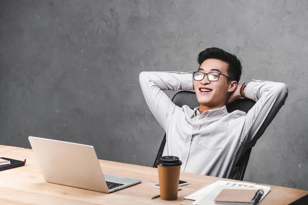 Sonriente asiático seo gerente sentado en mesa con cruzado los brazos - foto de stock