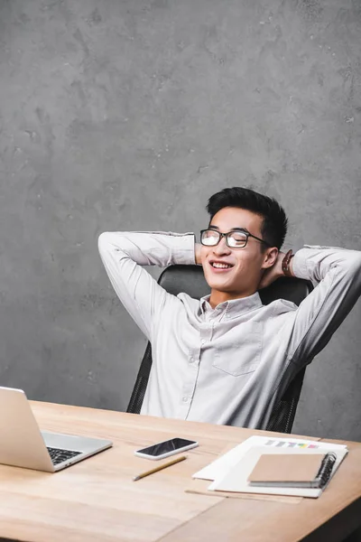 Lächelnder asiatischer SEO-Manager sitzt mit verschränkten Armen am Tisch — Stockfoto