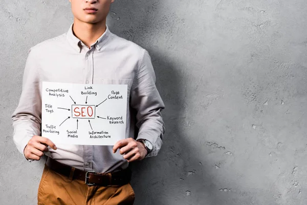 Cropped view of seo manager holding paper with concept words of seo — Stock Photo