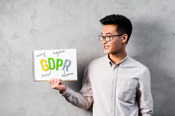 Sonriente asiático hombre de negocios celebración y mirando el papel con gdpr lettering - foto de stock