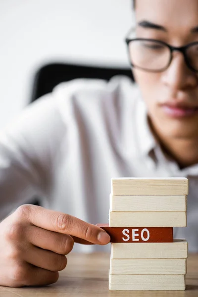 Foco seletivo de Asian seo manager segurando retângulo de madeira com letras seo — Fotografia de Stock