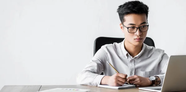 Panoramaaufnahme des asiatischen SEO-Managers mit Bleistift und Blick auf Laptop während des Webinars — Stockfoto