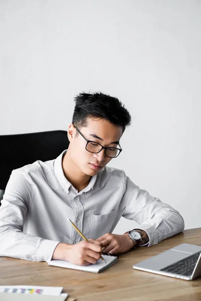 Азіатський сео менеджер, що пише в блокноті під час вебінару в офісі — стокове фото