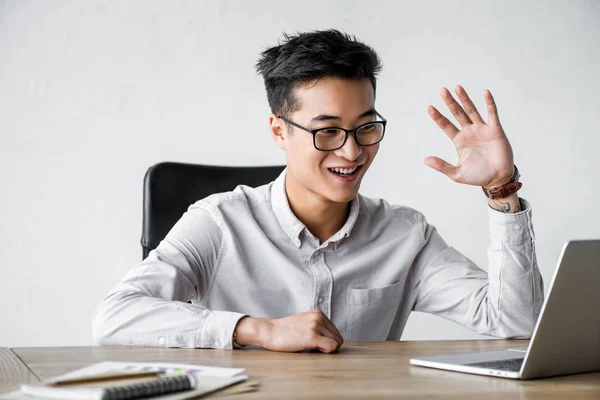 Sonriente asiático seo manager saludando durante webinar en oficina - foto de stock