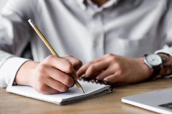 Cropped view of seo manager writing in notebook during webinar in office — Stock Photo