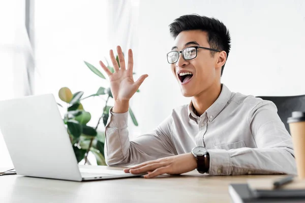 Sonriente asiático seo manager saludando durante webinar en oficina - foto de stock