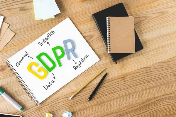 Top view of paper with gdpr lettering, notebooks, paper cup, pen, pencil, sticky notes, marker and crumpled papers on wooden table — Stock Photo