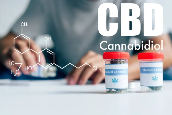 Selective focus of bottles with medical cannabis on table with man on background with cbd molecule illustration — Stock Photo