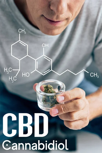 Cropped view of man in t-shirt looking at medical cannabis in glass container with cbd molecule illustration — Stock Photo