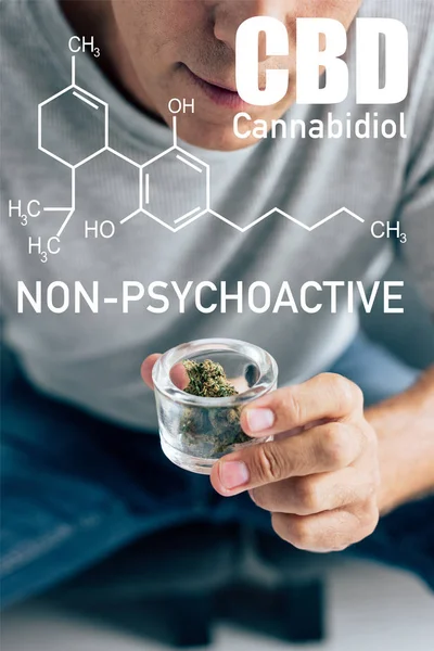 Обрезанный вид человека в футболке, смотрящего на медицинскую марихуану в стеклянном контейнере с непсихоактивной иллюстрацией CBD — стоковое фото