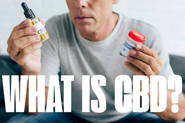 Cropped view of man in t-shirt holding medical cannabis and cbd oil in bottle with what is CBD question — Stock Photo