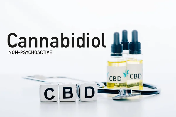 Cubes with cbd lettering near oil and stethoscope isolated on white with non-psychoactive cbd illustration — Stock Photo