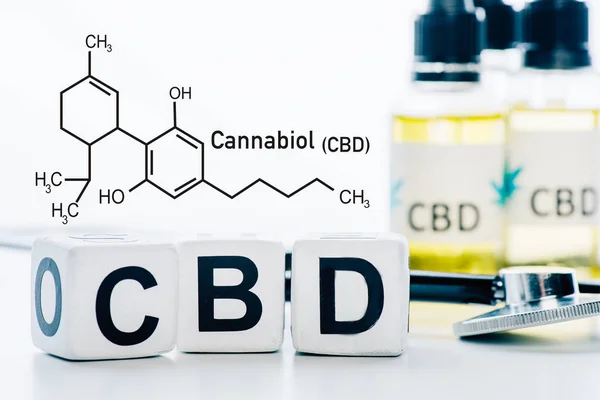 Selective focus of cubes with cbd lettering near oil and stethoscope isolated on white with cbd molecule illustration — Stock Photo