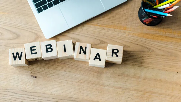 Cubos de madera con letras webinar cerca del ordenador portátil - foto de stock