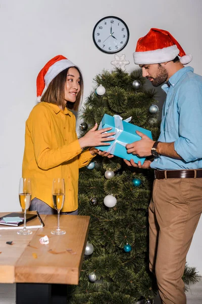 Happy bearded man giving present to asian woman in santa hat — Stock Photo