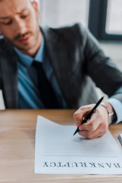 Selective focus of businessman holding pen near paper with bankruptcy letters — Stock Photo