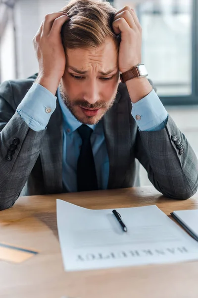 Selective focus of frustrated businessman looking at paper with bankruptcy letters — Stock Photo