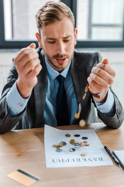 Selective focus of sad businessman throwing coins near paper with bankruptcy letters — Stock Photo