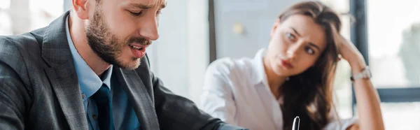 Panoramic shot of upset businessman near attractive businesswoman in office — Stock Photo