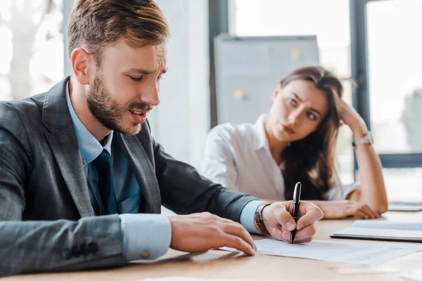 Selective focus of sad businessman holding pen near paper and attractive businesswoman in office — Stock Photo