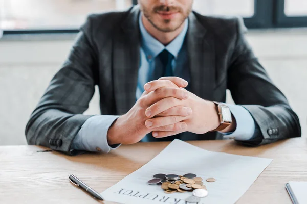 Ausgeschnittene Ansicht eines Geschäftsmannes, der mit geballten Händen neben Münzen und Dokument auf dem Tisch sitzt — Stockfoto