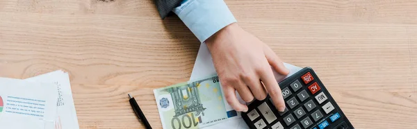 Panoramic shot of man using calculator near euro banknote — Stock Photo