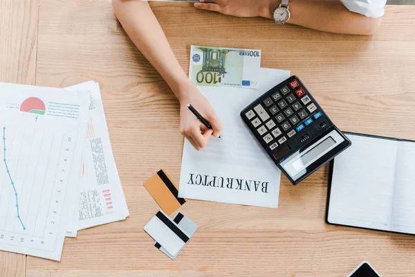 Top view of businesswoman signing document with bankruptcy letters near credit card and euro banknote — Stock Photo