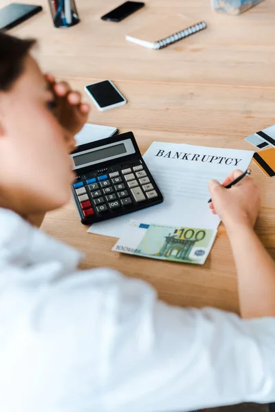 Selective focus of woman signing document with bankruptcy letters near credit cards and euro banknote — Stock Photo