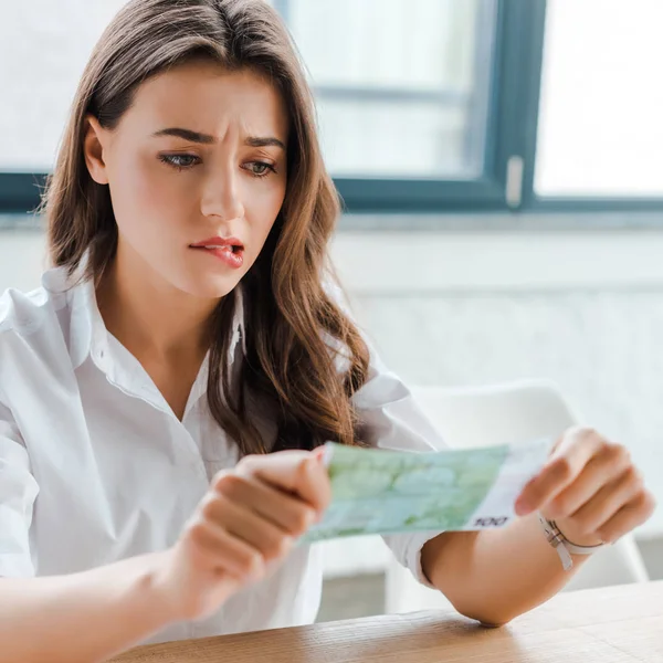 Selective focus of upset woman biting lips while looking at euro banknote — Stock Photo