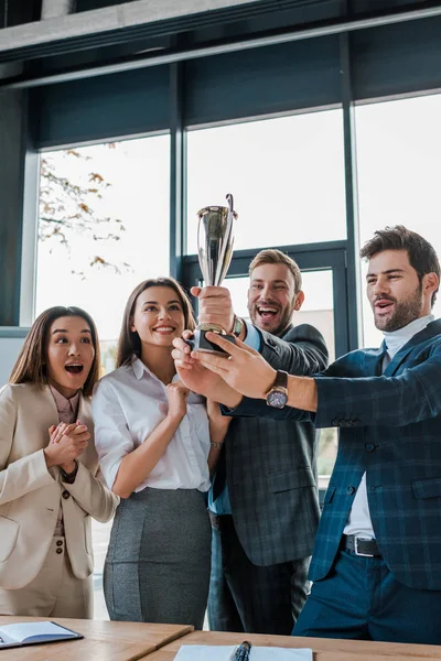 Heureuses femmes d'affaires multiculturelles et hommes d'affaires regardant trophée dans le bureau — Photo de stock