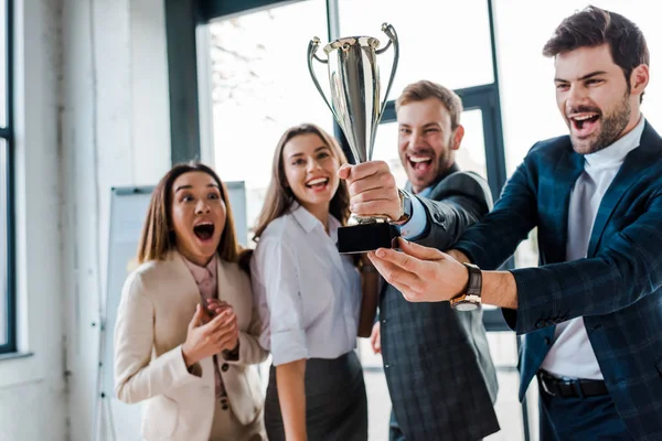 Selective focus of excited multicultural businesswomen and businessmen looking at trophy in office — Stock Photo