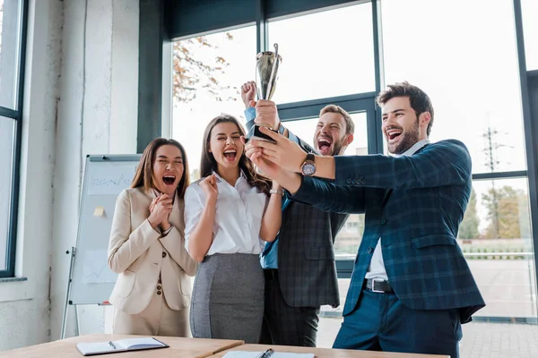 Happy businessmen and multicultural businesswomen holding trophy in office — Stock Photo