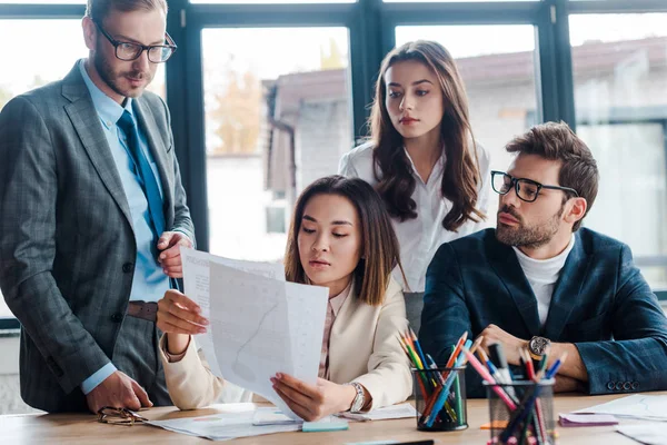 Selective focus of businessmen looking at documents near multicultural businesswoman in office — Stock Photo
